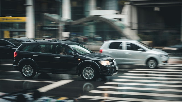 Black SUV driving past the pedestrian crosswalk. Your probability of getting into a car accident increases when speeding.
